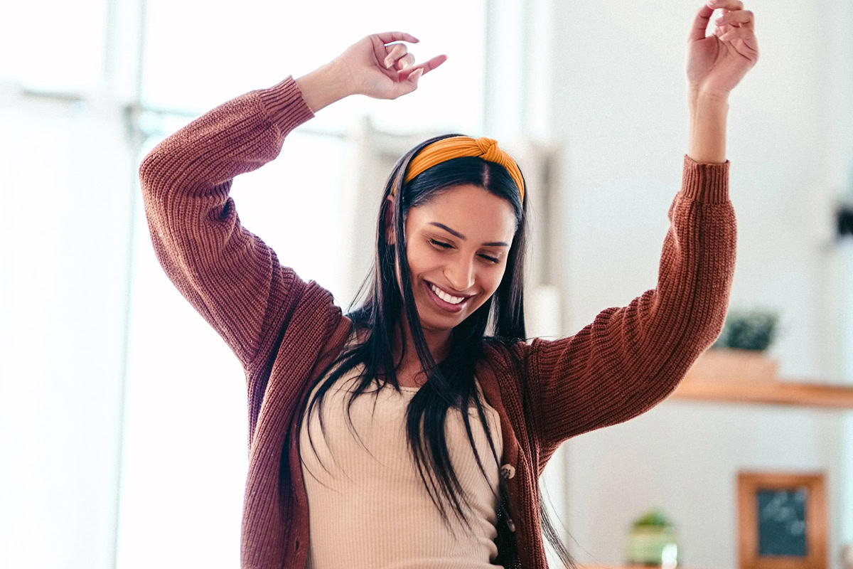 Person dancing in their home with hands in the air, smiling