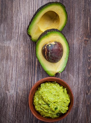 Guacamole dip and avocados on a board