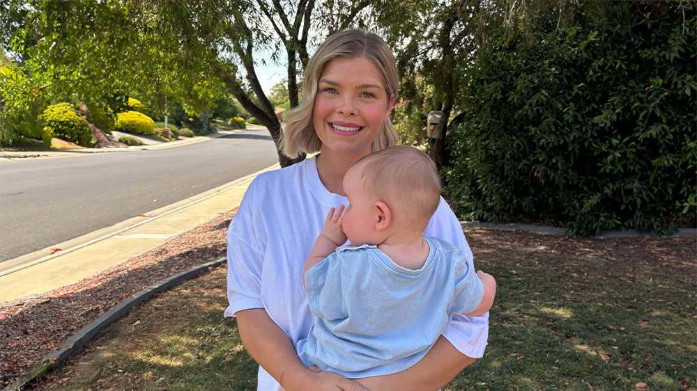 Caitlin Rogers holds baby Mac with trees in the background.