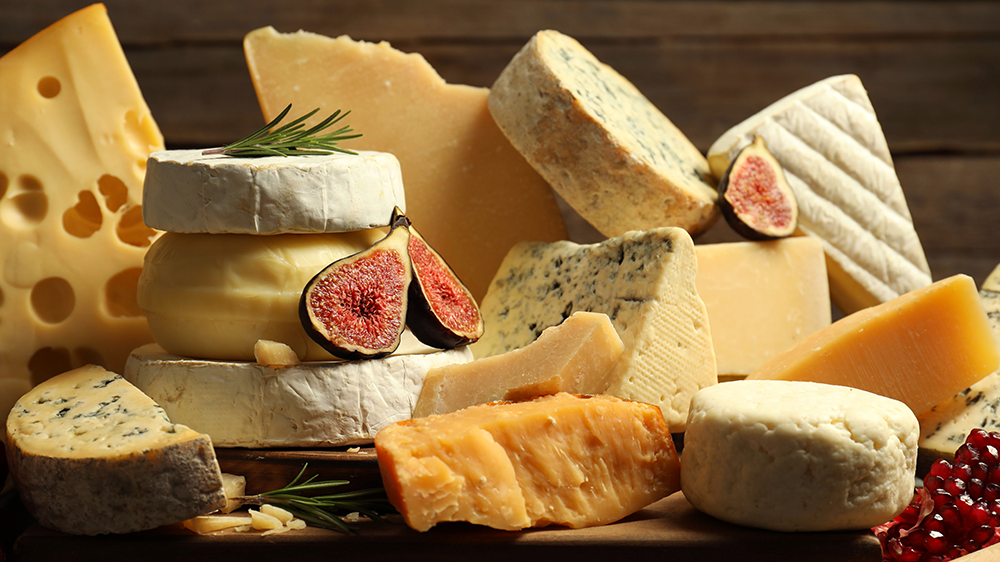 array of cheeses along with rosemary sprigs, figs and redcurrants against a dark background