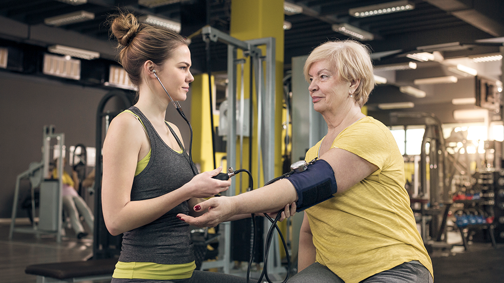 WOman in yellow top having her blood pressure tested in the gym by her younger trainer