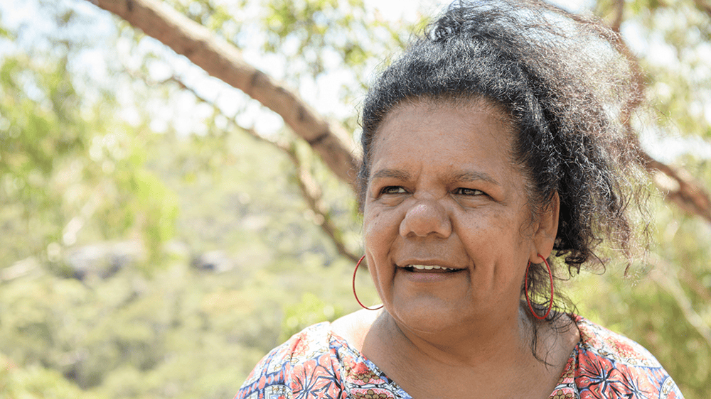 Indigenous woman standing outside with trees in background