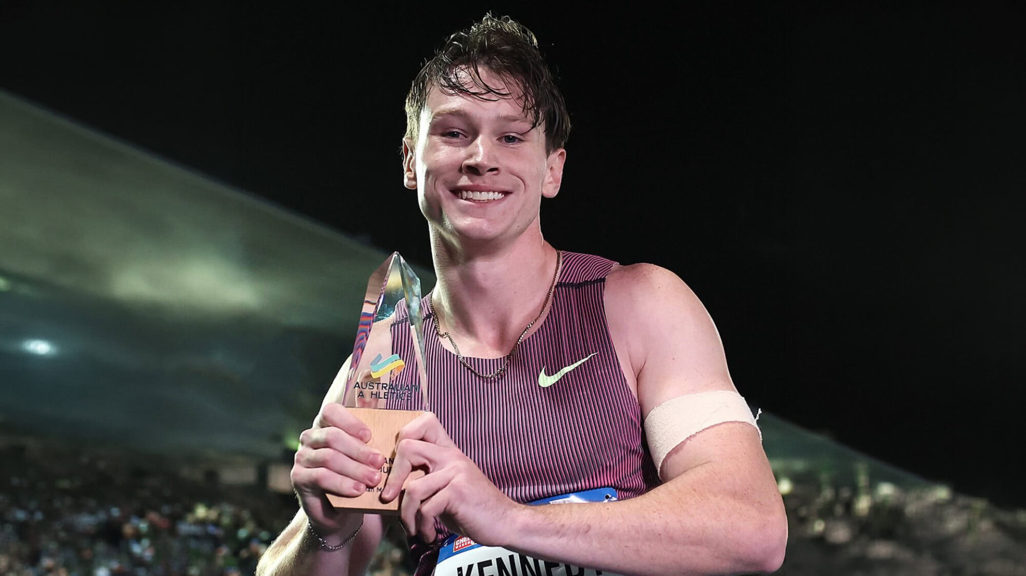 Lachie looks down at the camera while holding the Australian Athletics 100m Champion trophy.
