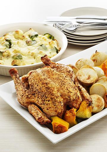 Roast chicken with roast vegetables and mashed potatoes in white serving dishes