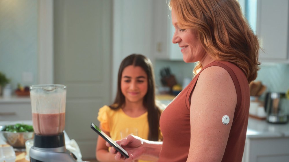 Freestyle Libre 3 Plus worn by a woman looking at a smart phone.