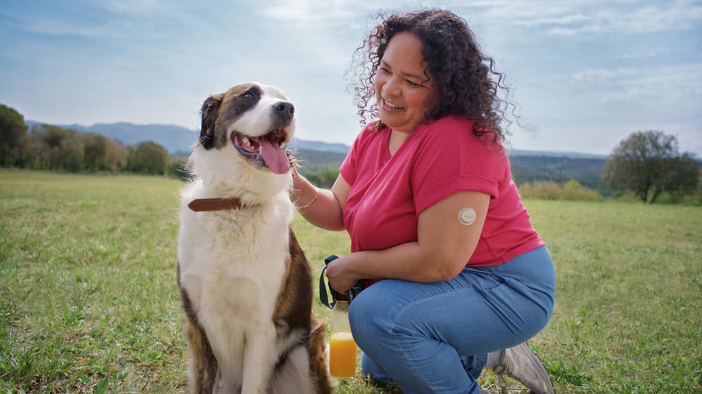 Woman who is outdoors with her dog, is using a CGM sensor on her arm