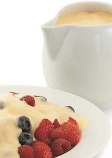custard and berries in a white bowl next to a pitcher of custard