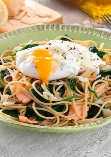 Spaghetti and salmon topped with a poached egg and fresh salmon on a green plate