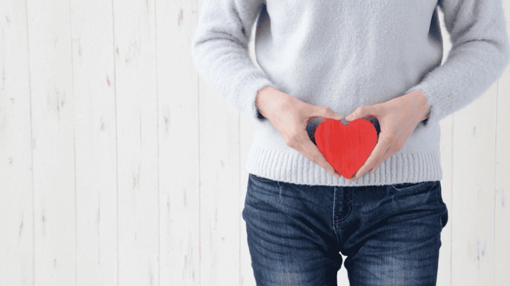 womens health, woman standing with a red heart in a grey jumper and blue jeans