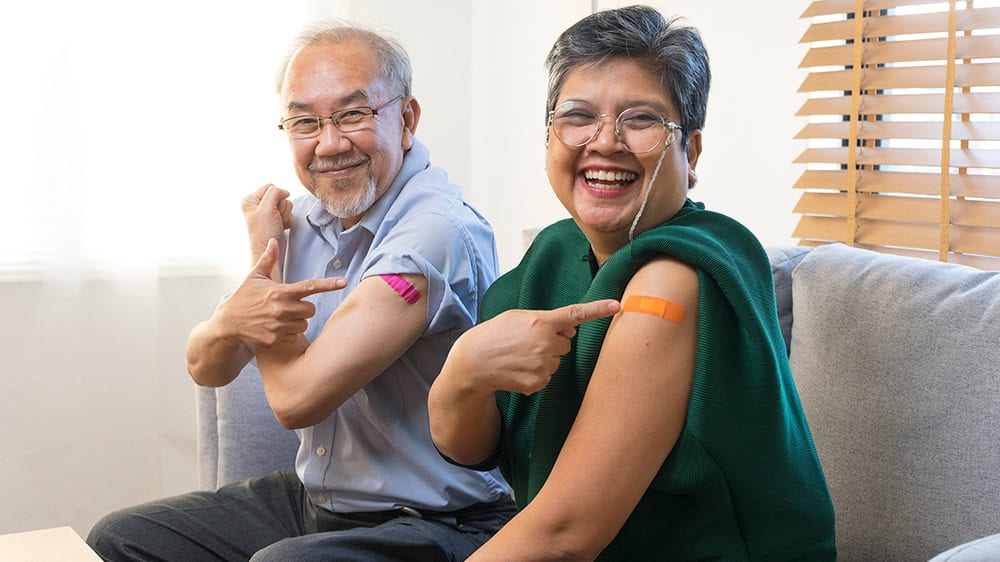 Two people, pointing to band-aids on their arms, have just received a vaccination.