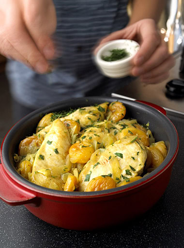 man sprinkling chopped parsley on to dish of Moroccan Chicken sitting on a gas hob