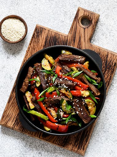 Beef and vegetable stir fry in a plate, resting on a cutting board