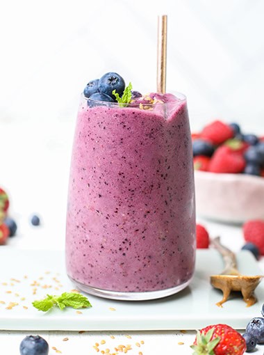 A vibrant purple smoothie shown with blueberries and strawberries.