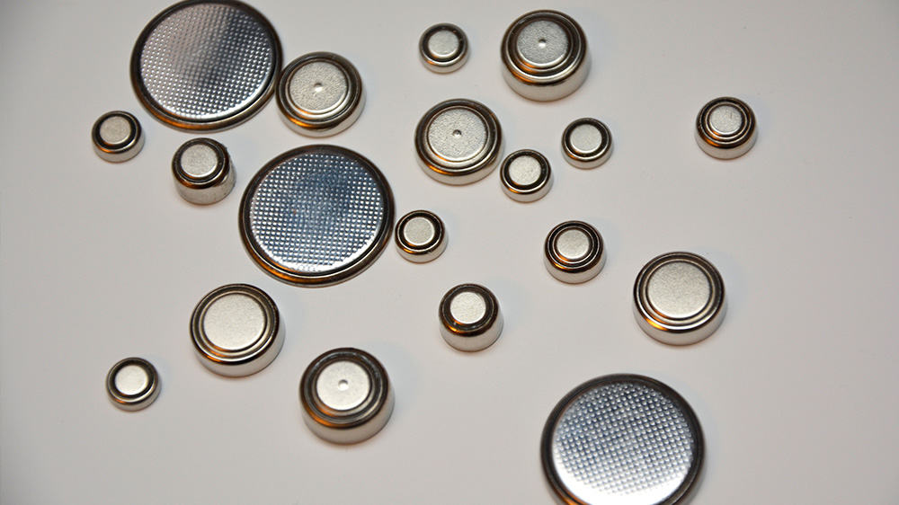 Selection of silver and gold button batteries on a cream coloured background