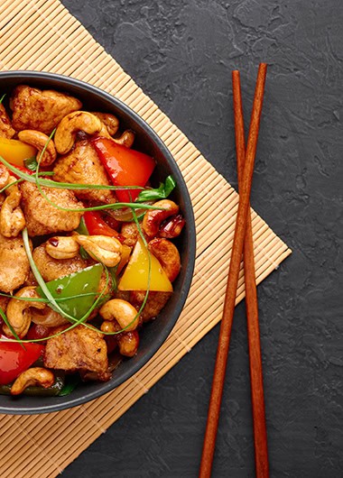 Gai Pad Med Mamuang or Thai Cashew Chicken in black bowl on dark slate backdrop.