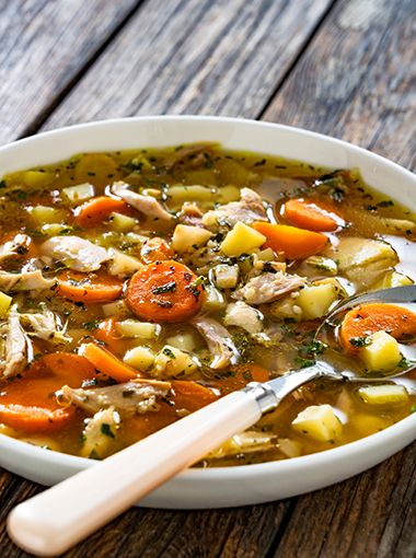 Chicken noodle soup in a bowl, resting on a wooden table