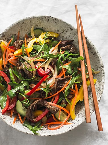 Warm asian style salad with beef and vegetables on a light background, top view