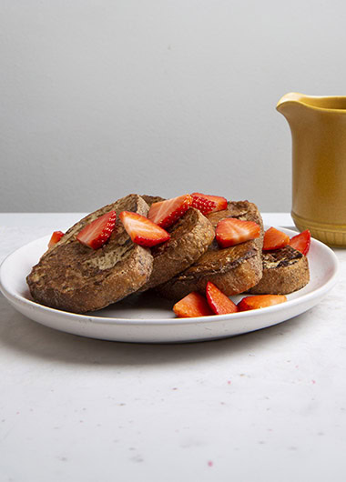French toast with strawberries on a white plate and yellow container with maple syrup