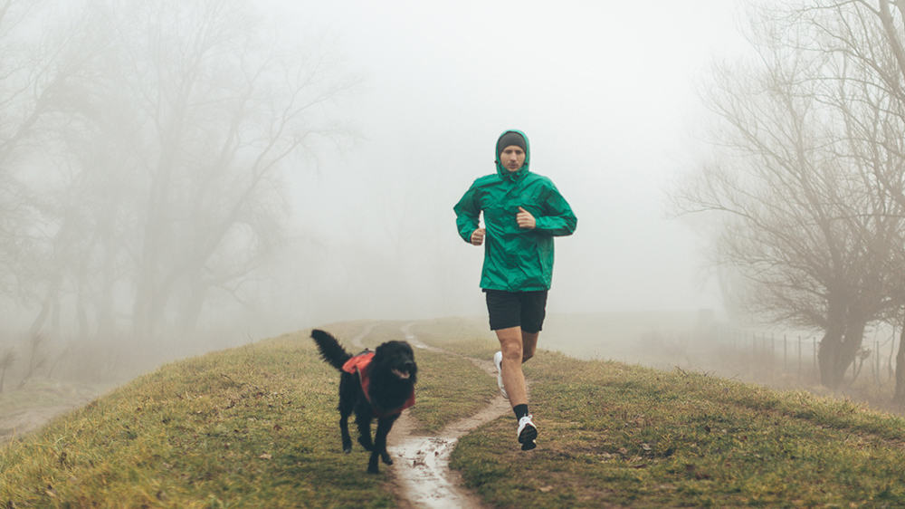 stay active this winter, man running on a cold damp and foggy day with dog in the countryside