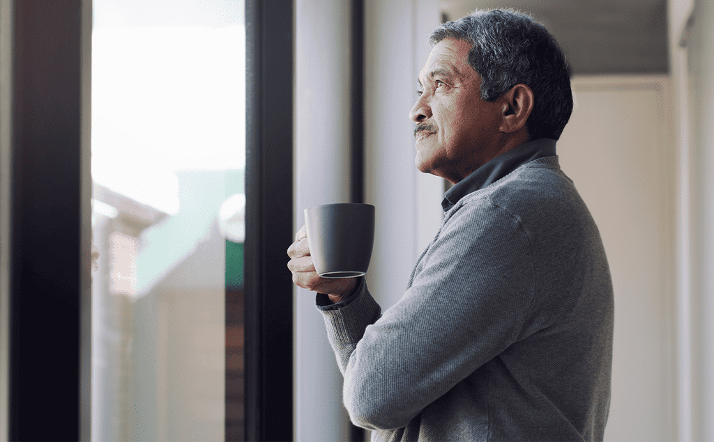 contemplative senior man looking out the window holding a cup of tea