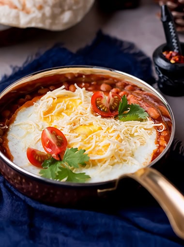 Baked Eggs with Baked Beans, Cheese and Tomato cooked in a frying pan on table side view of breakfast or brunch dish