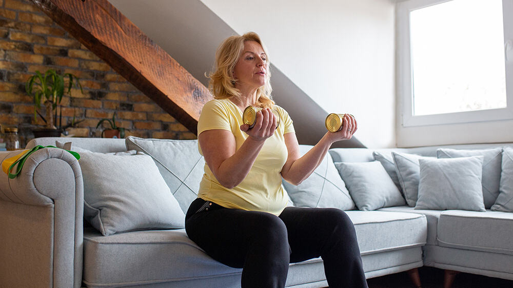middle-aged blond woman exercising at home using cans