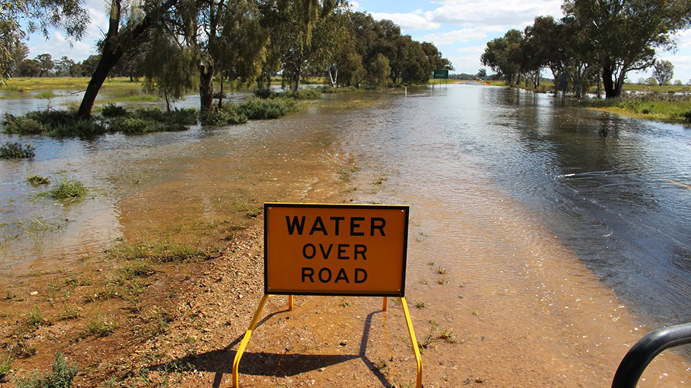 Water over road sign in front of flooded country road