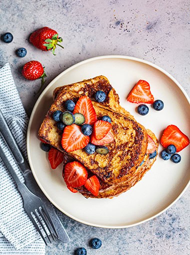 Traditional french toasts with blueberries and strawberries on a white plate.