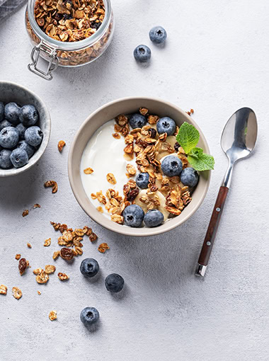 Yogurt, granola and fresh blueberry on a light background.