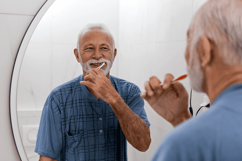older man brushing his teeth in the mirror