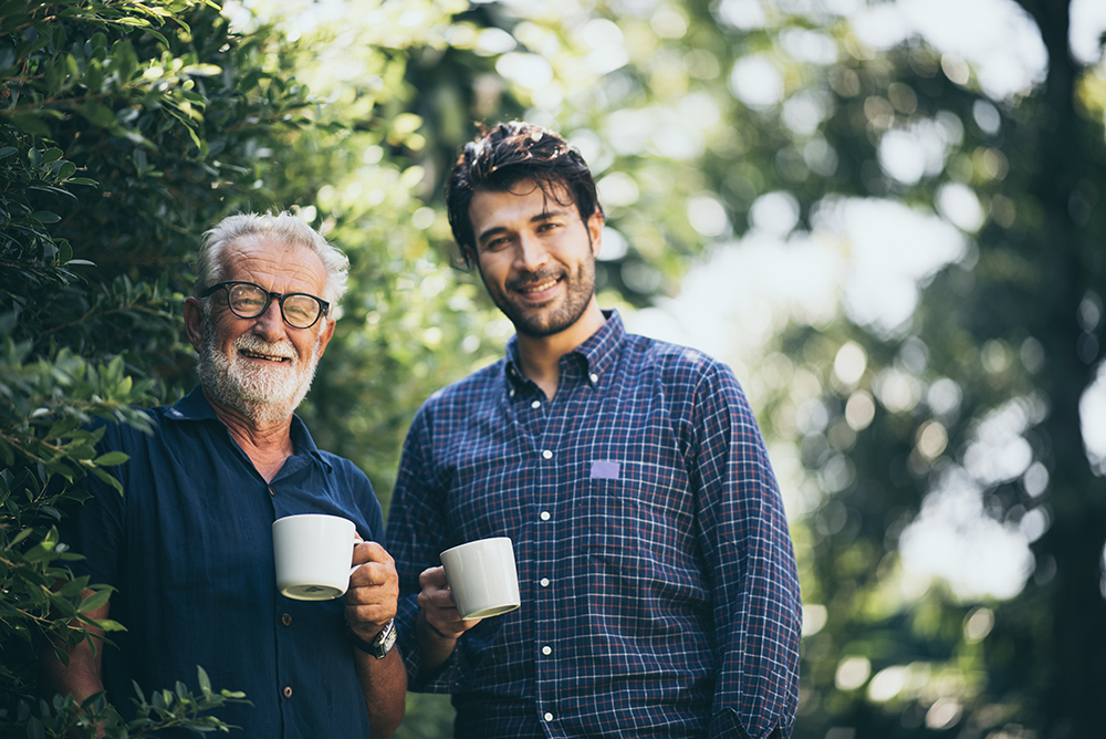 happy and relaxed father and adult son in the garden with a cup of tea