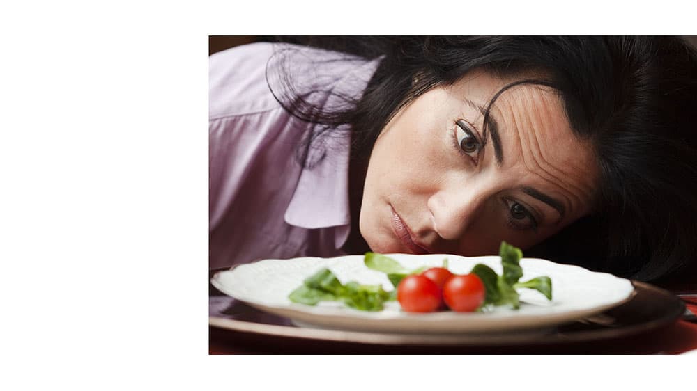 Dejected woman looking to a salad with sadness.