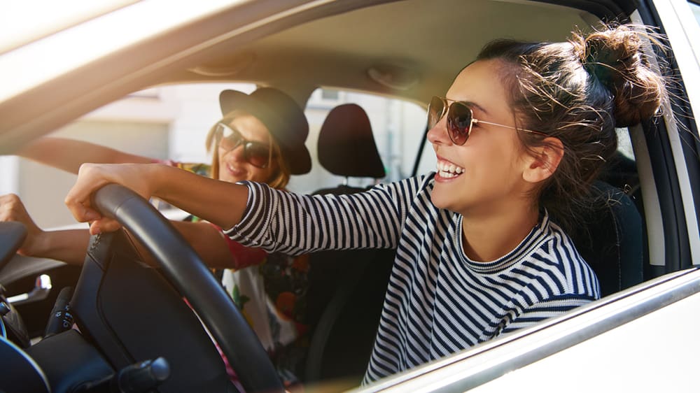 Two laughing young girlfriends driving together in a car