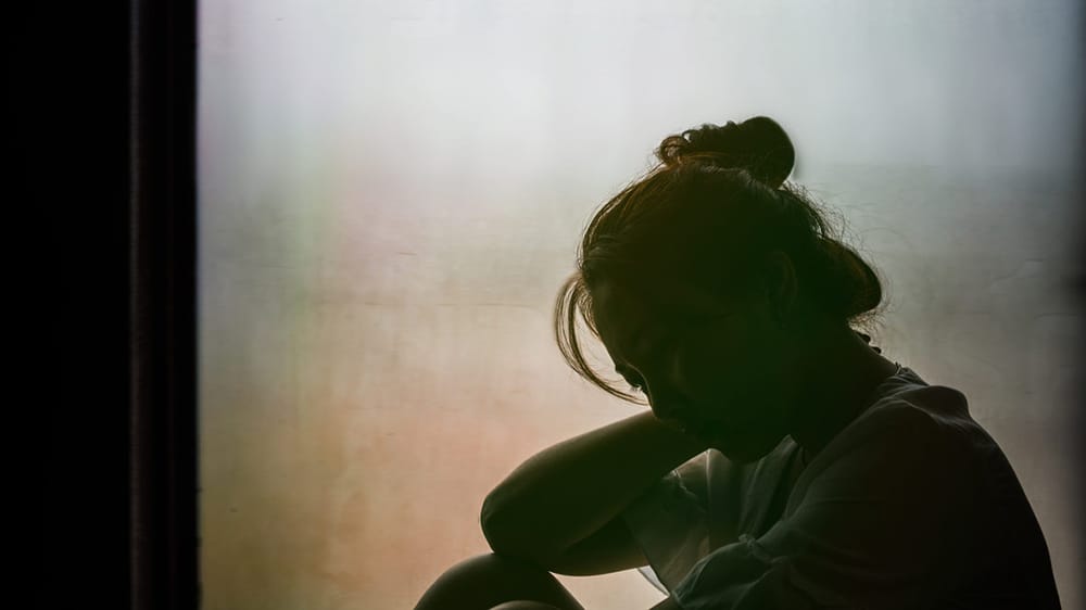 Vintage filtered on silhouette of depressed girl sitting on the window