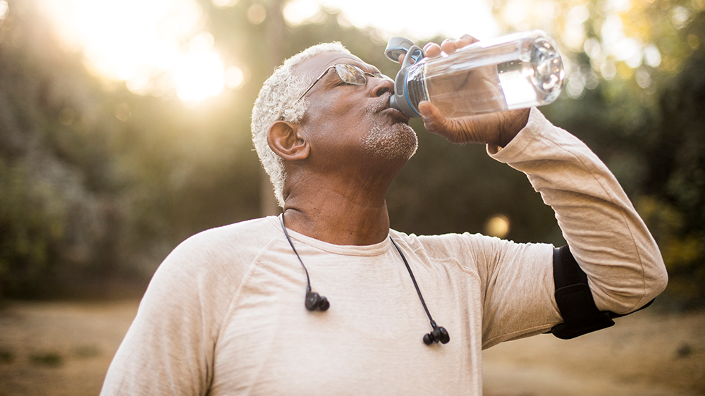 Older man who has been exercising drinking from a water bottle in a park