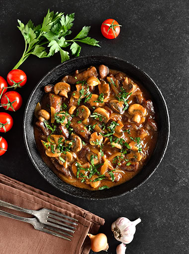 Tasty beef stroganoff with mushrooms in frying pan over black stone background.