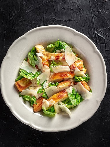 Chicken caesar salad with romaine and Parmesan cheese, top shot on a black background