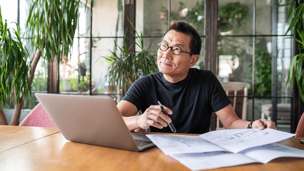 mature asian man with laptop thinking