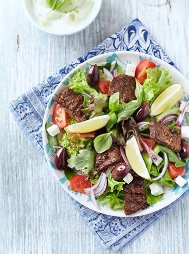 Tasty Salad with Grilled Beef Pieces, Cherry Tomatoes, feta Cheese and Kalamata Olives. Bright wooden background. Top view.