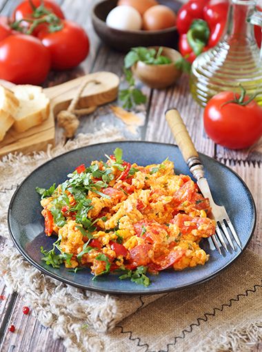 Mediterranean-inspired scrambled eggs on a plate, with a fork and other utensils and table settings around it
