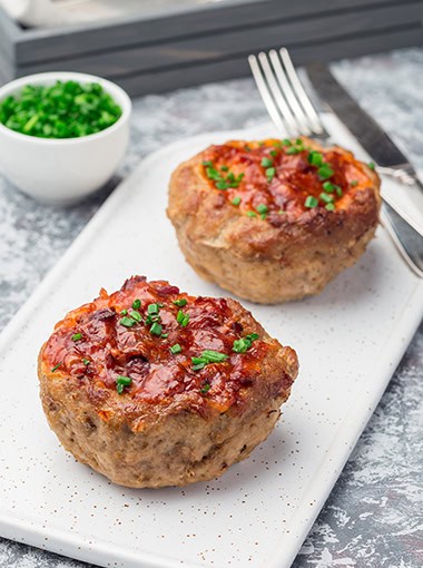 Low carb paleo meat cups, stuffed with champignons, bacon and cheese, garnished with green onion, on a white plate, vertical