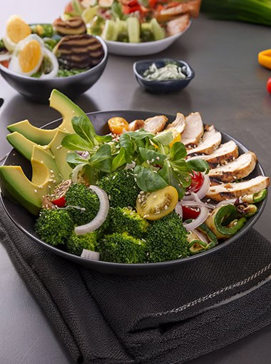 Salad of grilled chicken breast with broccoli, tomatoes and lamb's lettuce on a dark table.