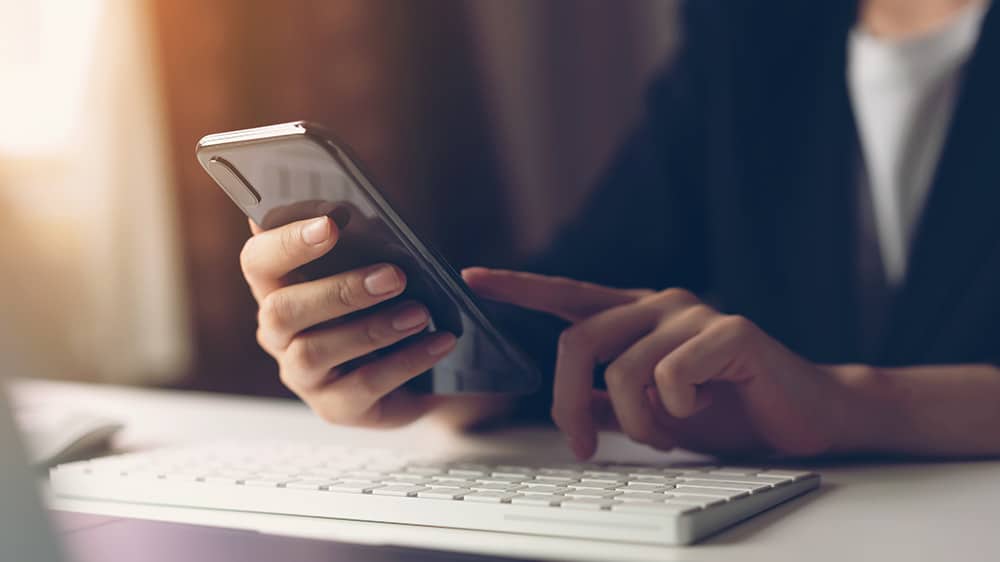 Close up of a person's hands using a phone app and a keyboard