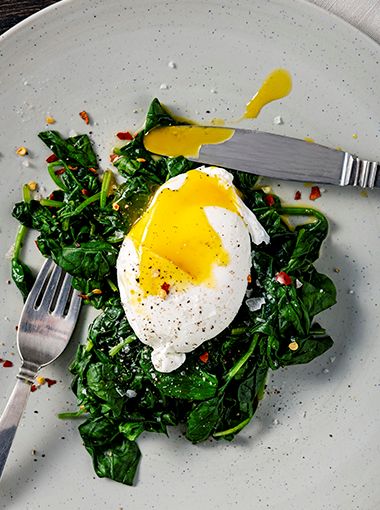 Poached eggs on greens, resting on plate with cutlery