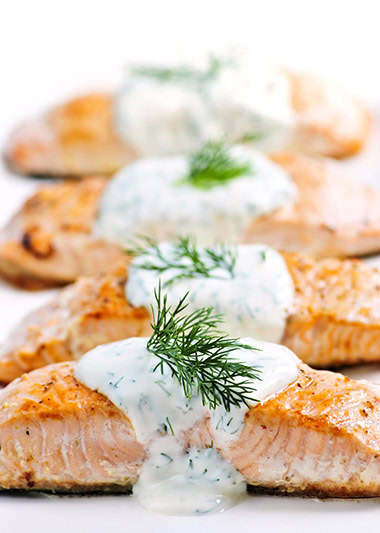 Cooked salmon fillets with dill sauce on white plate