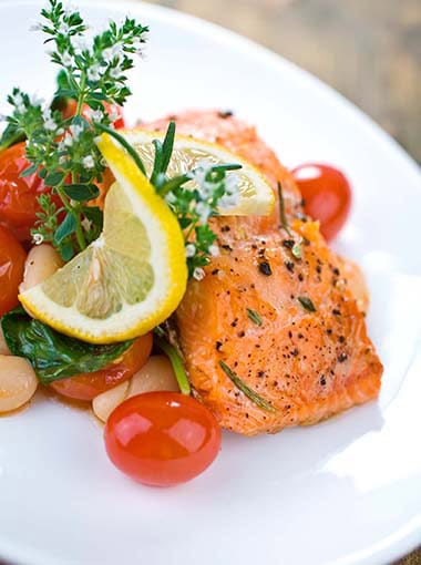 Baked Salmon topped with blooming herbs, lemon, and served with White bean, spinach and tomato salad.