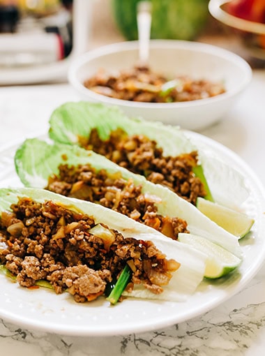 Ground Beef Lettuce Wraps on a plate with lime edges. These lettuce wraps are using romaine lettuce. Vertical Photo.