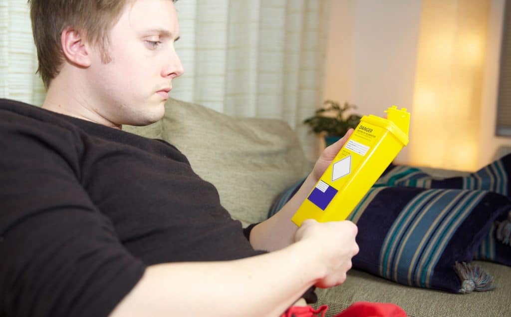 disposal of sharps, man on sofa inspecting yellow sharps bin