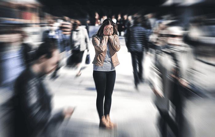 Stressed woman with head in hands standing in a busy street