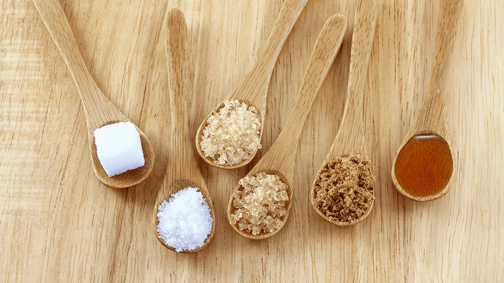 sugar and honey in wooden spoons on a wooden background